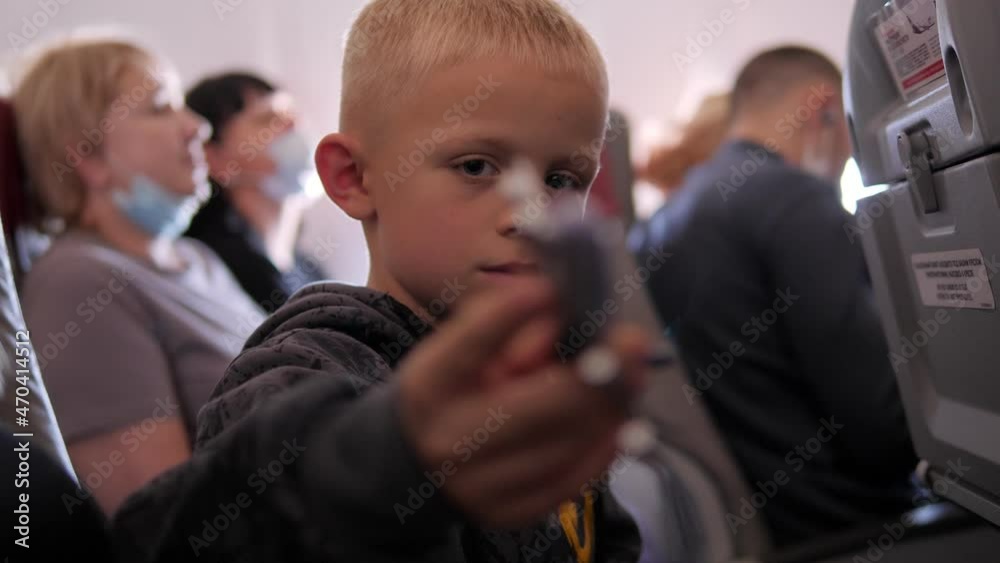 A little boy is sitting in an airplane in a chair with a toy airplane in his hands, he is playing during the flight, people are sitting in the background. A little boy is sitting in an airplane in a chair with a toy airplane in his hands, he is playing during the flight, people are sitting in the background.