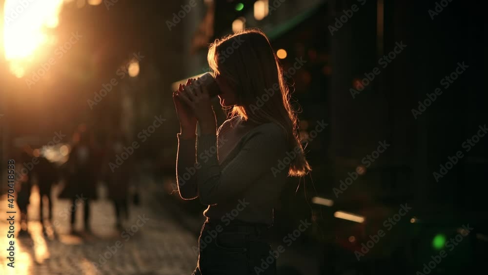 Silhouette of Happy young hipster woman drinking coffee at sunrise. Girl taking a sip of coffee or tea from wooden eco cup on warm summer evening sunset in big city. Natural beauty pretty woman