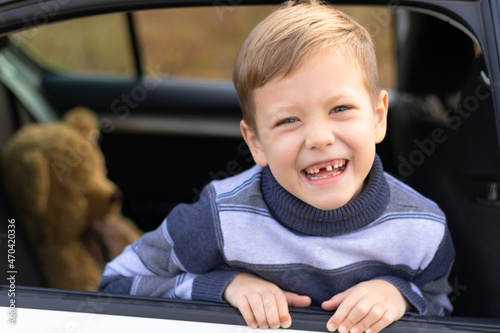 A seven year old cute boy leans out the window of a white car on a warm sunny autumn day against the backdrop of yellow foliage. Selective focus. Portrait