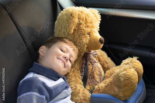 Seven year old cute boy with a toy bear in a car salon on a warm sunny autumn day. Selective focus. Portrait