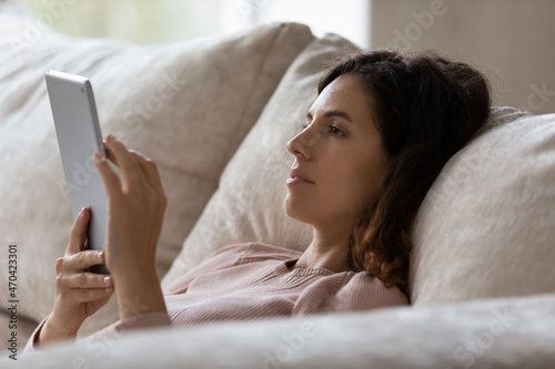 Close up profile of woman using tablet device, relaxing on couch at home, beautiful young female looking at gadget screen, chatting with friends in social network, surfing internet, watching video