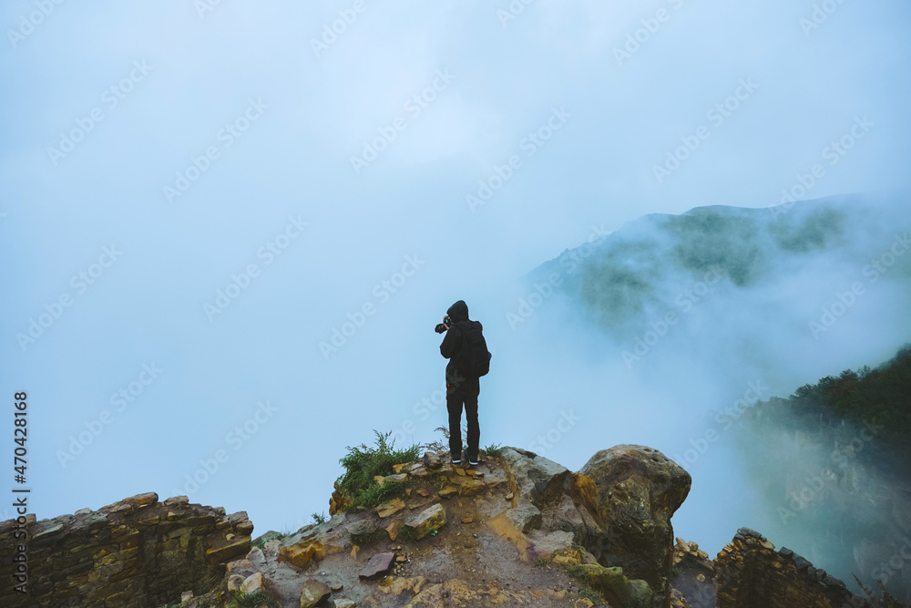 A guy stands at a cliff high in the mountains and photographs the fog