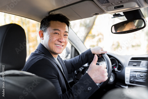 A man driving an Asian car behind the wheel looks at the camera and smiles © Liubomir