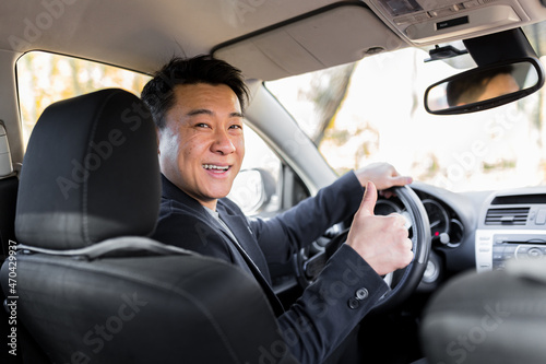 Successful businessman car salesman Male Asian driver behind the wheel looking into the camera and smiling