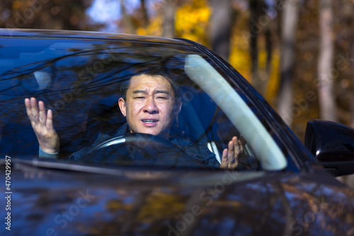 Furious angry asian man standing in a traffic jam beeps and hurries. Sitting in the car. Irritated young business male tired driver in automobile. Stressful commuting to be late work