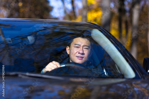 A pensive Asian man is sitting in the car, the driver is waiting and sad