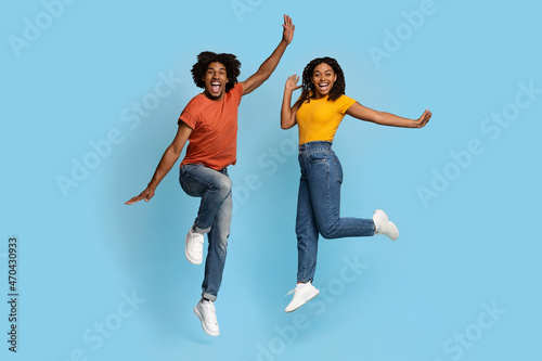 Happy african american lovers jumping over blue studio background