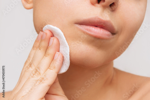 Cropped shot of a young caucasian woman cleaning her face with cotton pad on a white background. Skin care, cosmetology. Evening routine. The girl washes off her makeup with a cleanser. Close up