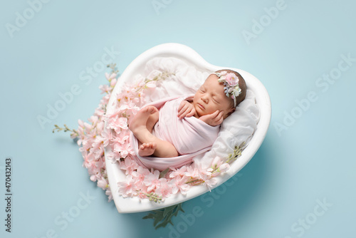 Newborn baby girl sleeping on a crib in the shape of a heart on a blue background. Newborn baby