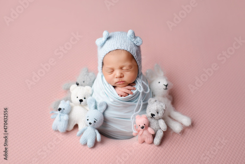 Sleeping newborn baby girl wrapped in a blue blanket surrounded by toys.