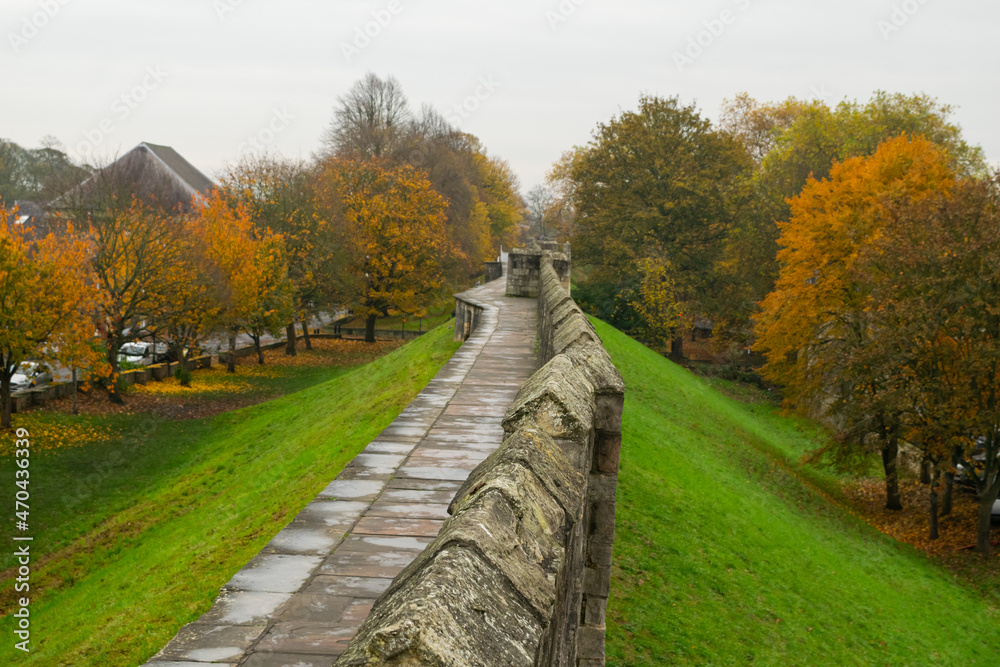 Part of trail at top of medieval 13th century stone city wall through colorful autumn foliage in York England