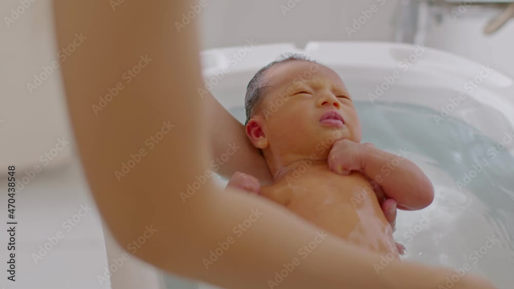 Calm of asian newborn baby bathing in bathtub.mother bathing her son in warm water.adorable newborn infant smile in tub relax and comfortable.Newborn baby care concept Calm of asian newborn baby bathing in bathtub.mother bathing her son in warm water.adorable newborn infant smile in tub relax and comfortable.Newborn baby care concept