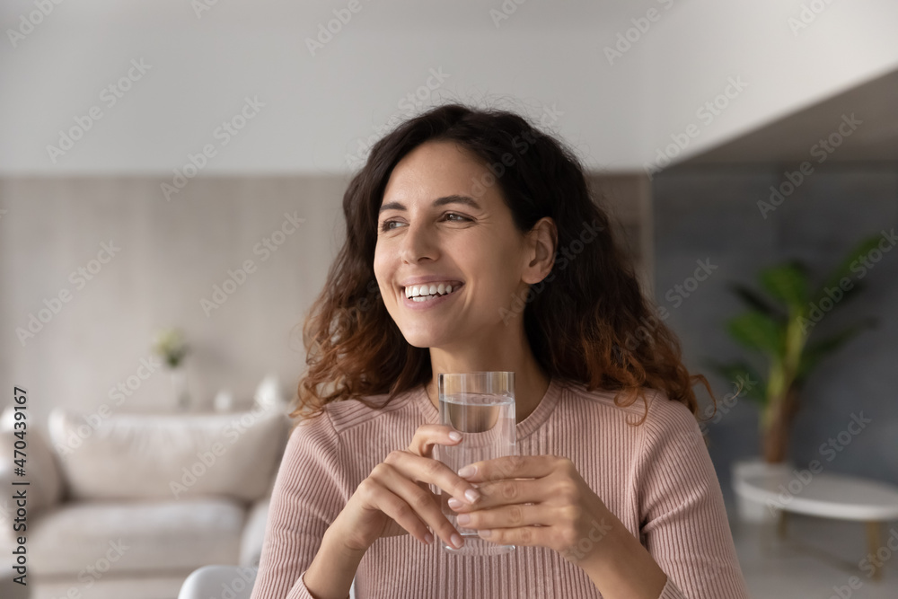 Head shot smiling dreamy woman holding glass of pure clean mineral water looking in distance visualizing, excited positive beautiful young female enjoying healthy lifestyle habit, refreshment concept Head shot smiling dreamy woman holding glass of pure clean mineral water looking in distance visualizing, excited positive beautiful young female enjoying healthy lifestyle habit, refreshment concept