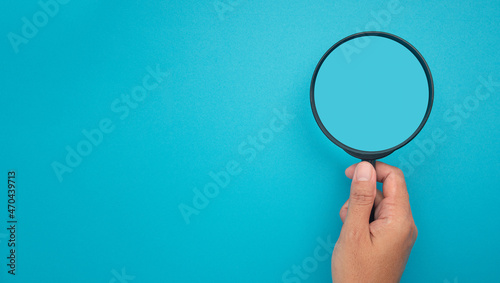 Hand holding of a magnifying glass over a blue background with space for text