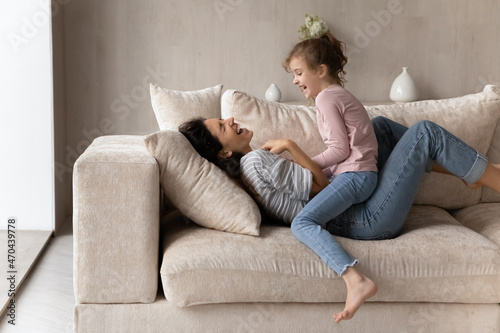 Photos Excited woman with little daughter playing relaxing on cozy couch engaged in fun