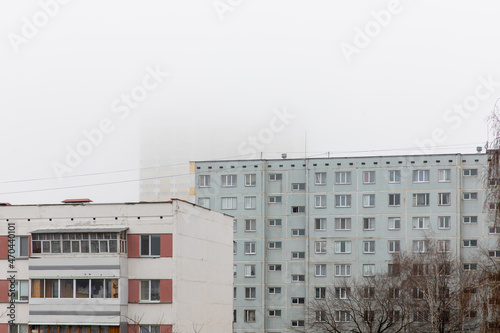 Foggy morning in a residential area of the city. In the background, a high-rise building is hidden in dense fog. 