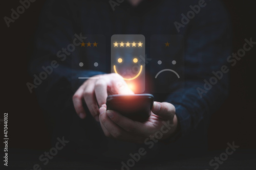 Businessman using smartphone for select smiley face icon for client evaluation and customer satisfaction after use product and service concept. photo
