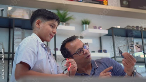 Indian father and son choosing eyeglasses in optics store
