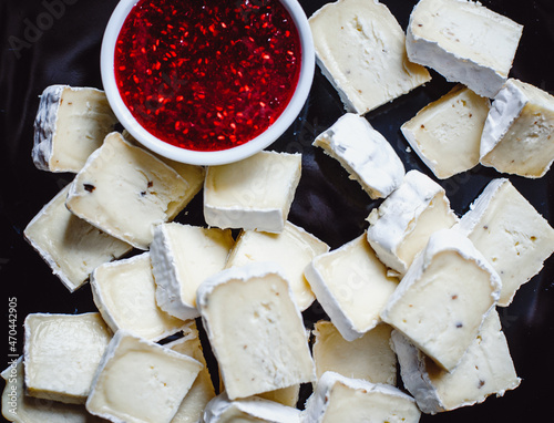 French soft cheese with white mold served with red raspberry jam on a black plate, closeup. Cheese composition. photo