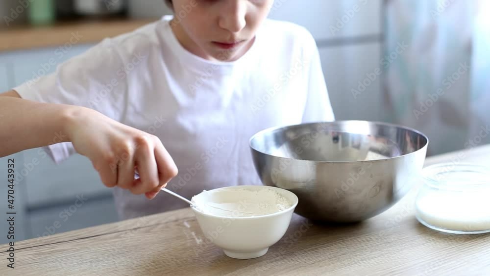 Child cooking at the kitchen. boy stirring dough for a cake in the steel bowl and adds flour to the dough. Child cooking at the kitchen. boy stirring dough for a cake in the steel bowl and adds flour to the dough.