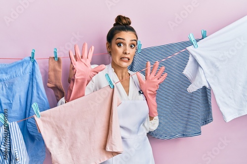 Beautiful brunette young woman washing clothes at clothesline afraid and terrified with fear expression stop gesture with hands, shouting in shock. panic concept.