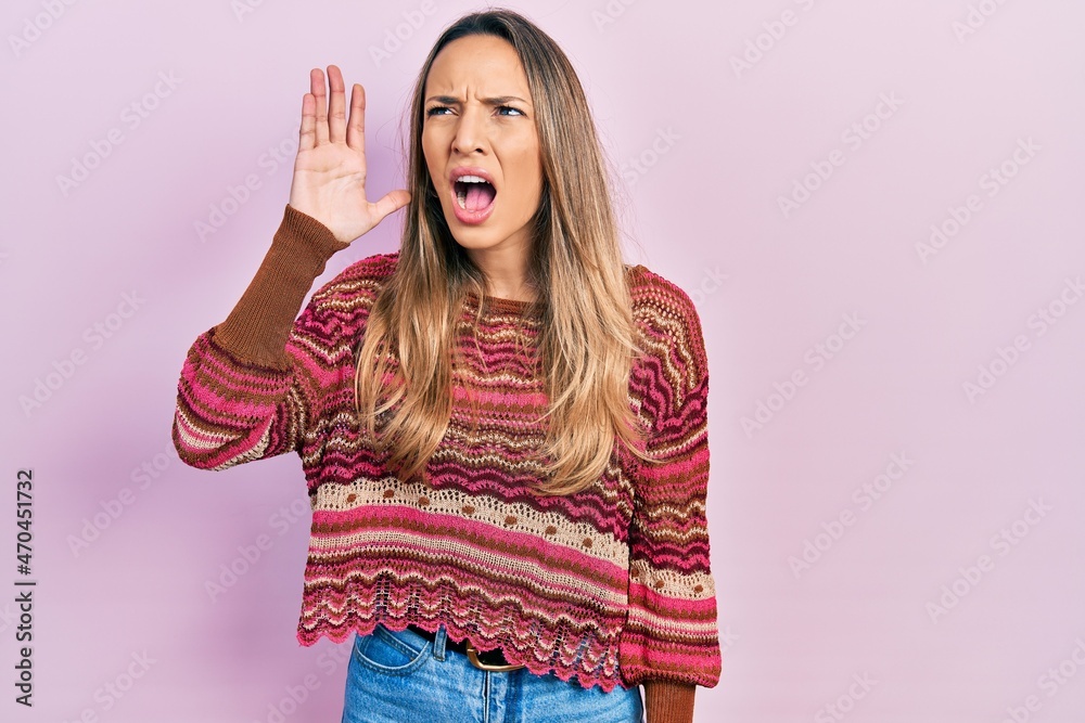 Beautiful hispanic woman wearing hippie sweater shouting and screaming loud to side with hand on mouth. communication concept.