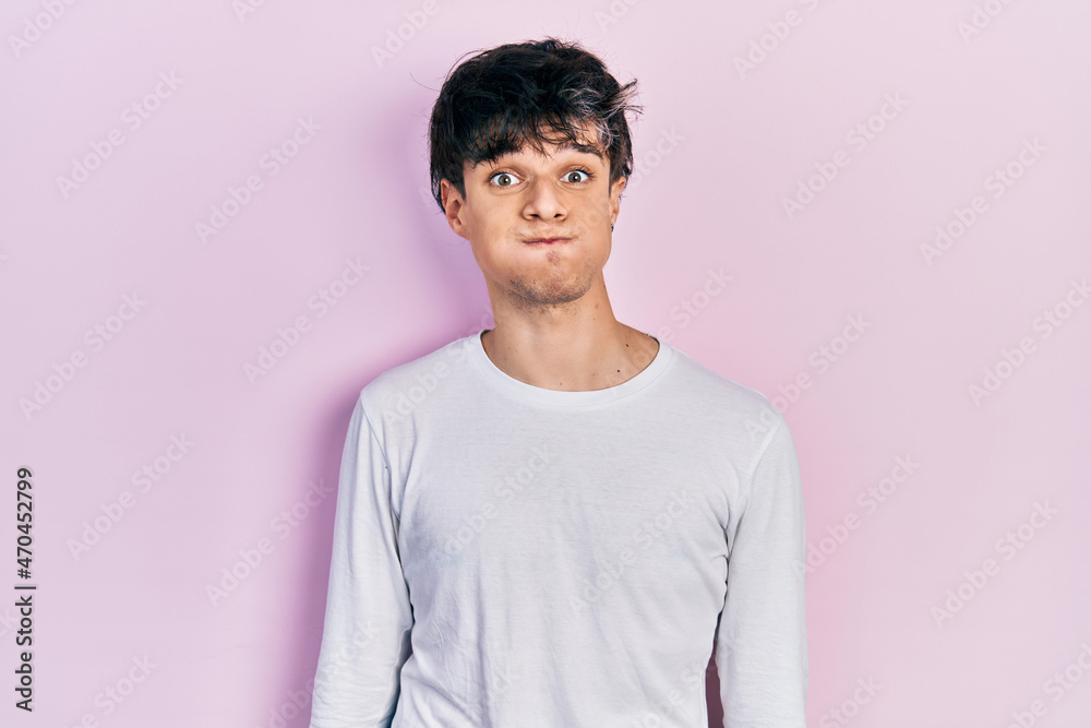 Handsome hipster young man wearing casual white shirt puffing cheeks with funny face. mouth inflated with air, crazy expression. - obrazy, fototapety, plakaty 