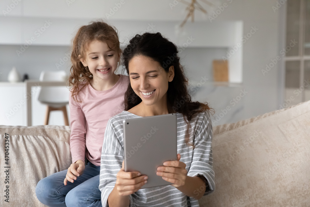Close up happy mother with adorable daughter using tablet together, looking at screen, smiling young mom and cute girl kid chatting online by video call, having fun with electronic device at home Close up happy mother with adorable daughter using tablet together, looking at screen, smiling young mom and cute girl kid chatting online by video call, having fun with electronic device at home