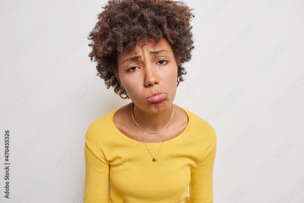 Doleful sad woman purses lips looks unhappily stands upset or moody faces problems dressed in casual yellow jumper isolated over white background has disappointed face. Negative emotions concept Doleful sad woman purses lips looks unhappily stands upset or moody faces problems dressed in casual yellow jumper isolated over white background has disappointed face. Negative emotions concept