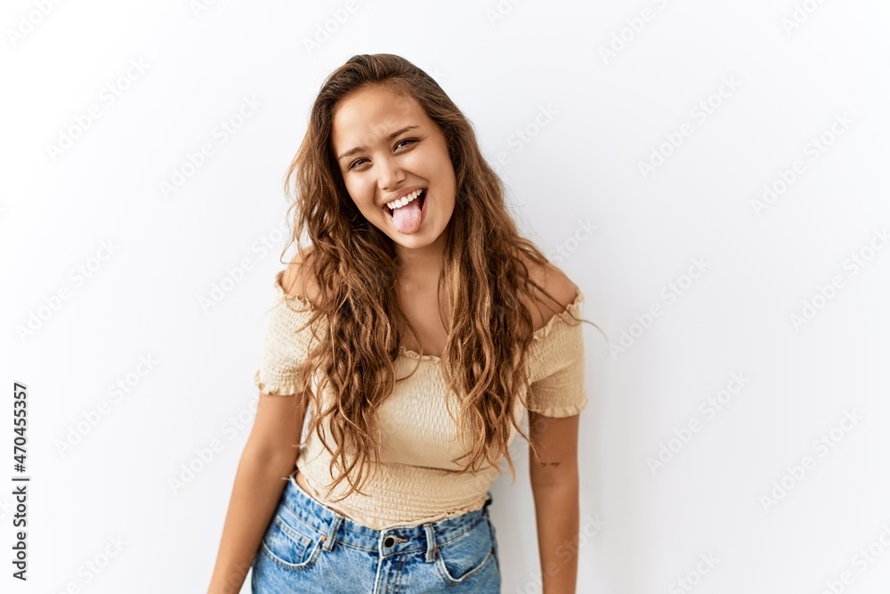 Beautiful hispanic woman standing over isolated while background sticking tongue out happy with funny expression. emotion concept. Beautiful hispanic woman standing over isolated while background sticking tongue out happy with funny expression. emotion concept.