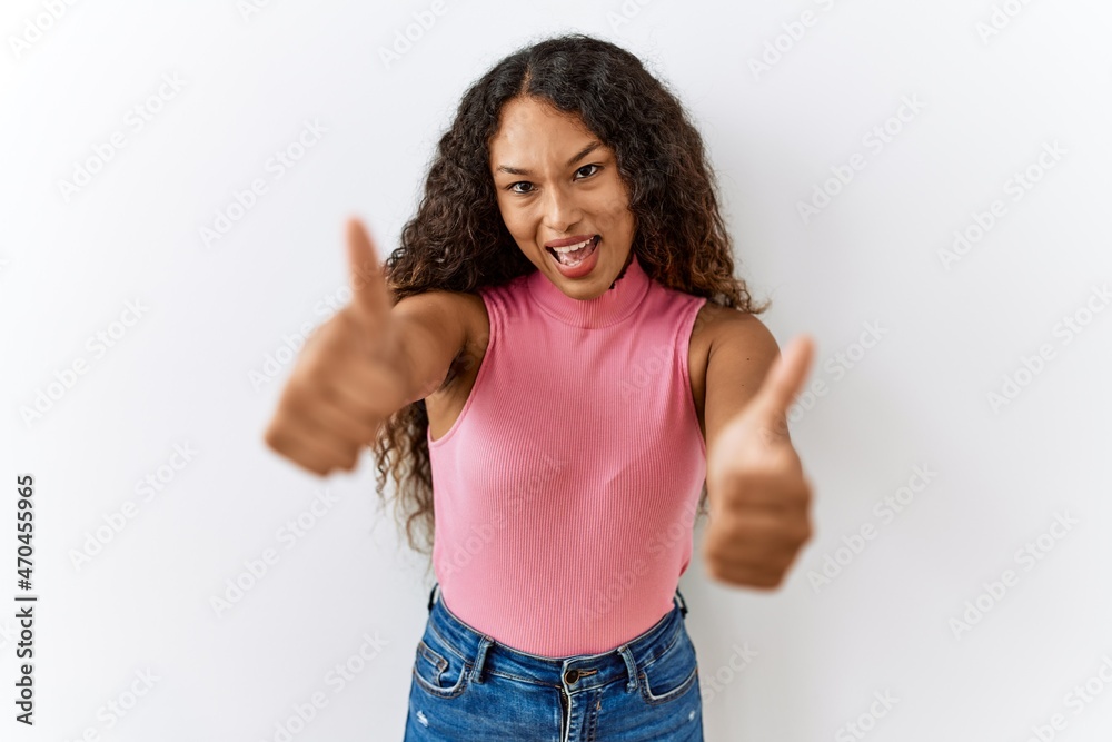 Beautiful hispanic woman standing over isolated background approving doing positive gesture with hand, thumbs up smiling and happy for success. winner gesture. Beautiful hispanic woman standing over isolated background approving doing positive gesture with hand, thumbs up smiling and happy for success. winner gesture.