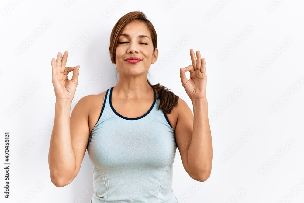 Young latin woman wearing sporty clothes over isolated background relax and smiling with eyes closed doing meditation gesture with fingers. yoga concept. Young latin woman wearing sporty clothes over isolated background relax and smiling with eyes closed doing meditation gesture with fingers. yoga concept.
