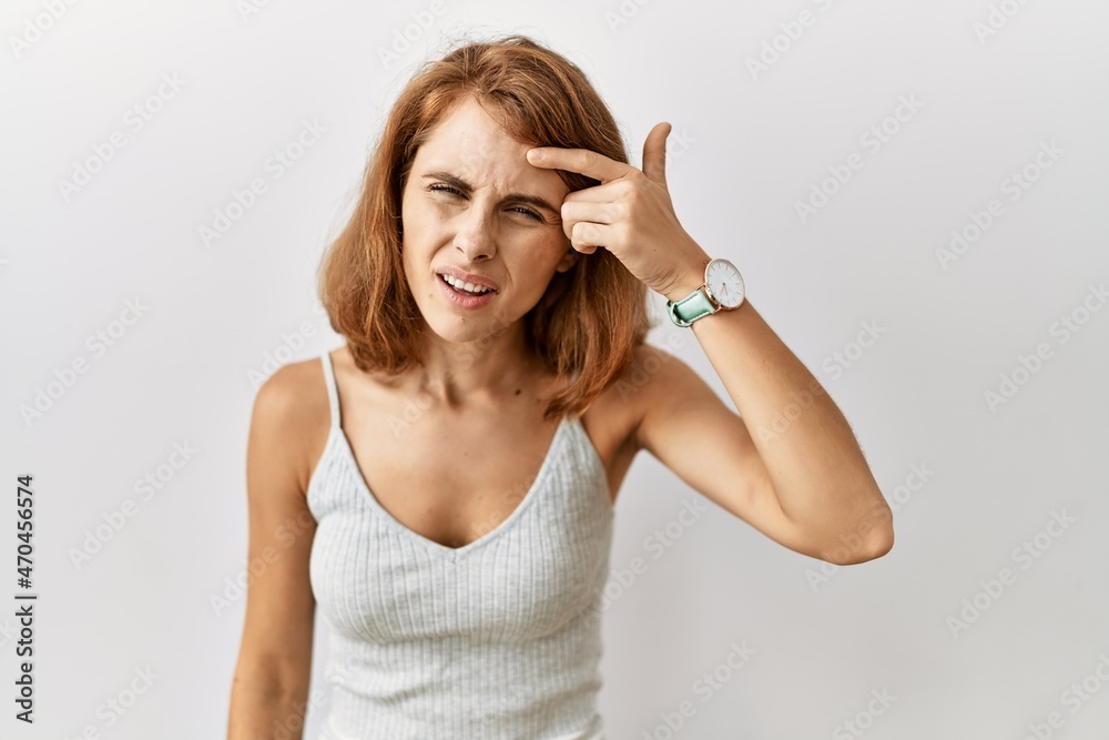 Beautiful caucasian woman standing over isolated background pointing unhappy to pimple on forehead, ugly infection of blackhead. acne and skin problem