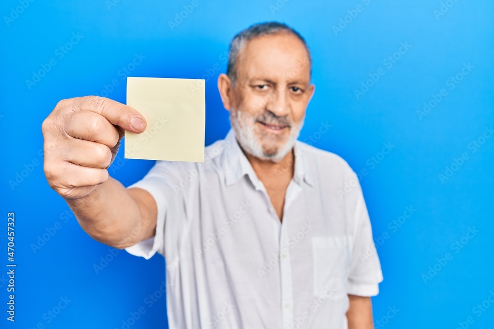Handsome senior man with beard holding paper reminder looking positive and happy standing and smiling with a confident smile showing teeth Handsome senior man with beard holding paper reminder looking positive and happy standing and smiling with a confident smile showing teeth