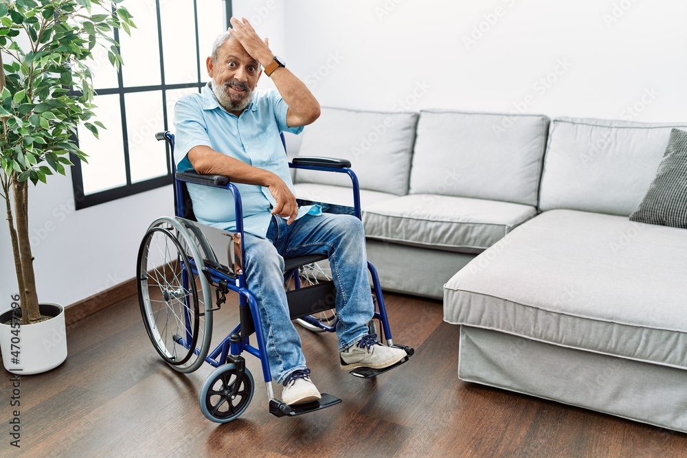 Handsome senior man sitting on wheelchair at the living room surprised with hand on head for mistake, remember error. forgot, bad memory concept. Handsome senior man sitting on wheelchair at the living room surprised with hand on head for mistake, remember error. forgot, bad memory concept.