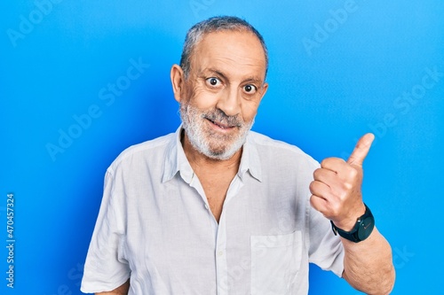 Handsome senior man with beard wearing casual white shirt smiling with happy face looking and pointing to the side with thumb up.
