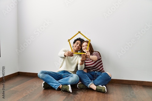 Young hispanic couple holding house project sitting on the floor at empty new home. photo