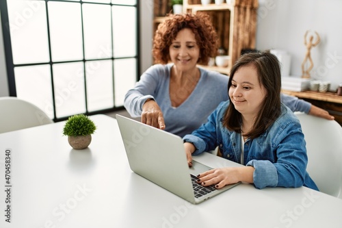 Leinwand Poster Mature mother and down syndrome daughter using computer laptop at home