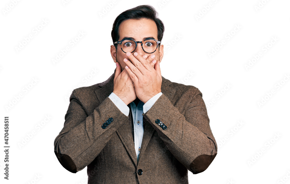 Young hispanic man wearing business jacket and glasses shocked covering mouth with hands for mistake. secret concept. Young hispanic man wearing business jacket and glasses shocked covering mouth with hands for mistake. secret concept.