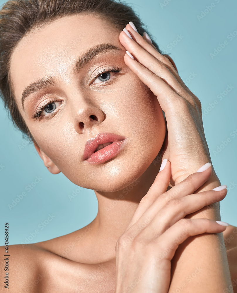 Naklejka premium Skin care. Beautiful woman with healthy facial skin touching her moisturized face skin, on blue background. High quality