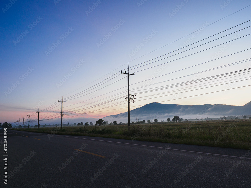 Country road at sunrise and electric wires with blue sky, mountains in the background