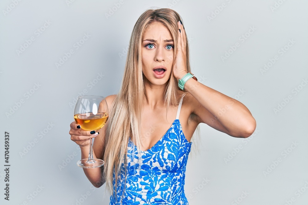 Young beautiful caucasian woman drinking a glass of white wine afraid and shocked, surprise and amazed expression with hands on face Young beautiful caucasian woman drinking a glass of white wine afraid and shocked, surprise and amazed expression with hands on face
