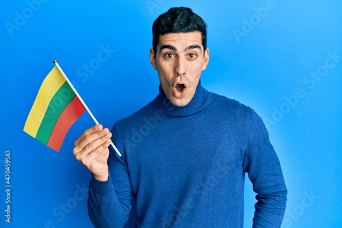 Handsome hispanic man holding lithuania flag scared and amazed with open mouth for surprise, disbelief face