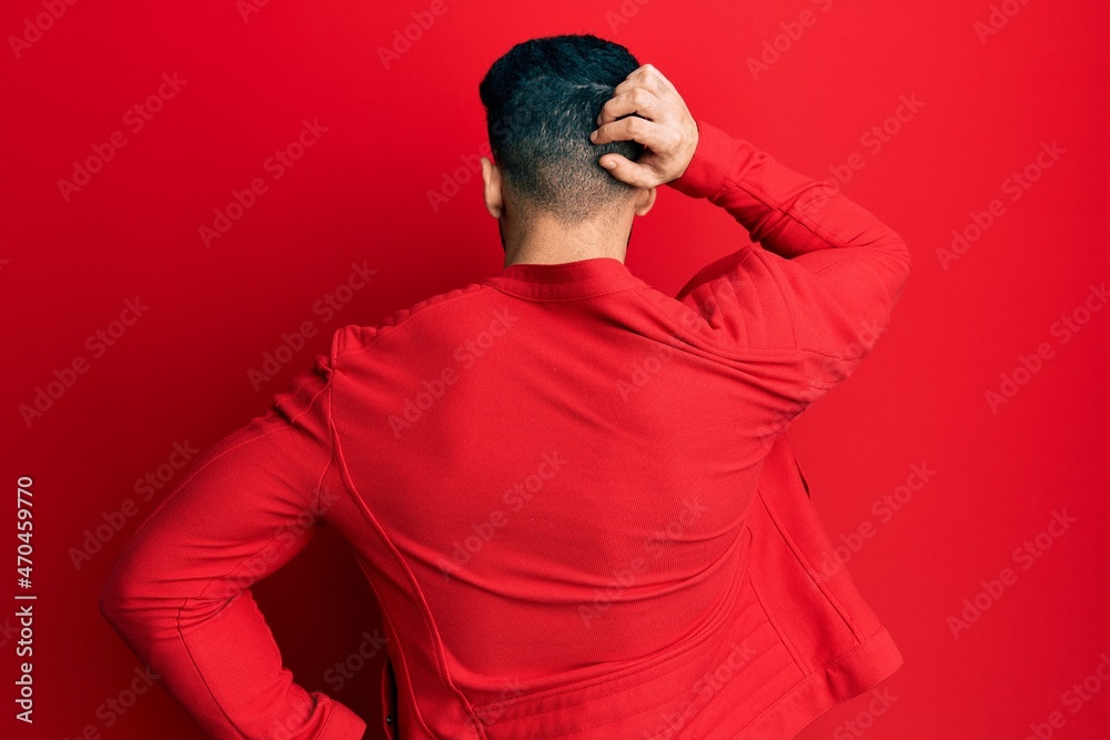 Young hispanic man wearing red leather jacket backwards thinking about doubt with hand on head