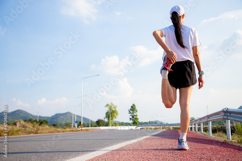 Young woman stretching before running while looking for beautiful landscape on roadside. Sports and Recreation
