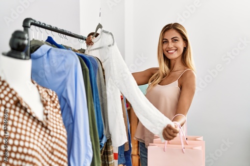 Young caucasian customer woman smiling happy holding hanger with clothes at clothing store.