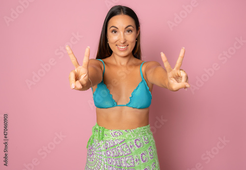 Young beautiful woman on vacation wearing bikini over isolated pink background doing peace symbol with fingers.