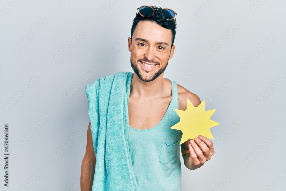 Young hispanic man wearing summer style holding yellow sun looking positive and happy standing and smiling with a confident smile showing teeth