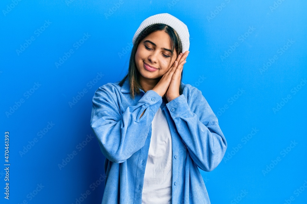 Young latin woman wearing cute wool cap sleeping tired dreaming and posing with hands together while smiling with closed eyes. Young latin woman wearing cute wool cap sleeping tired dreaming and posing with hands together while smiling with closed eyes.