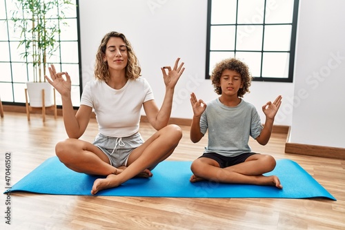 Young woman and son sitting on training mat at the gym relax and smiling with eyes closed doing meditation gesture with fingers. yoga concept.